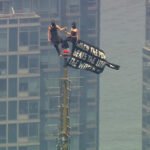 2 personer klatrer til toppen av Empire State Building-spiret, trer ut et banner